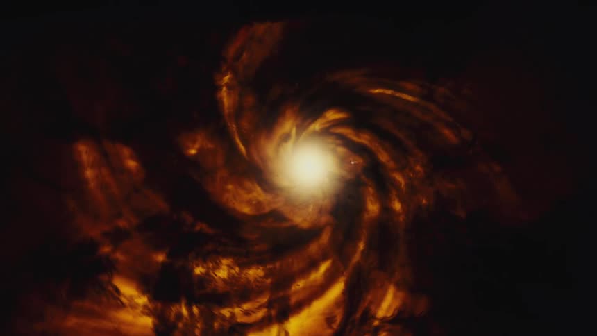 A fiery golden spiral nebula slowly rotates in deep space, with a bright star glowing intensely at its core