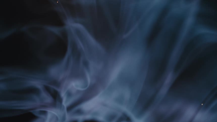 Ethereal blue-tinted smoke swirls and billows gracefully against a dark background in slow motion