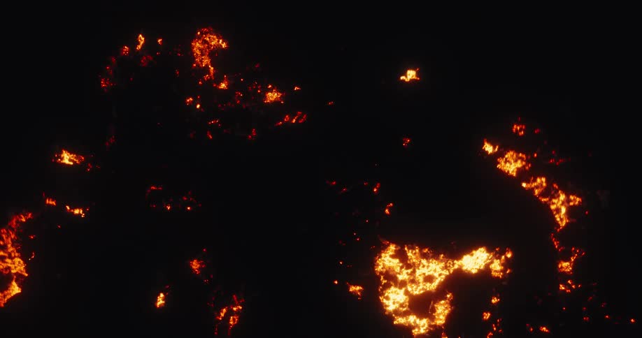 A slow, wide aerial shot reveals the destructive glow of a smoldering forest fire at night