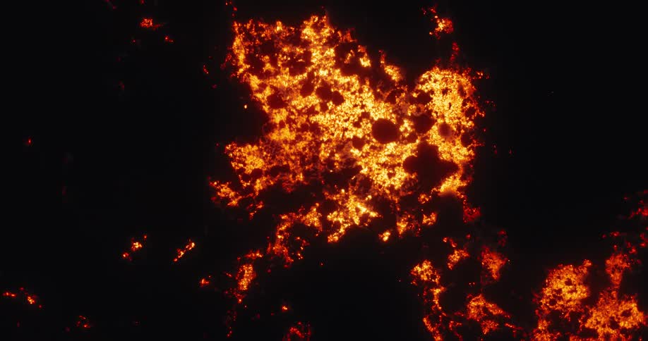 Abstract top-down aerial view of a fiery, smoldering landscape glowing against the blackness of night