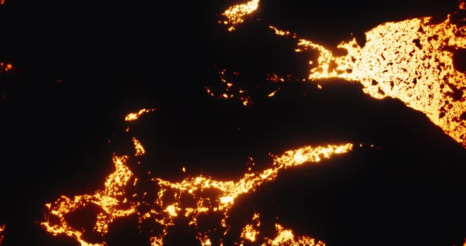 A close-up view of bright orange lava cracking through the hardened black surface of a volcanic flow at night