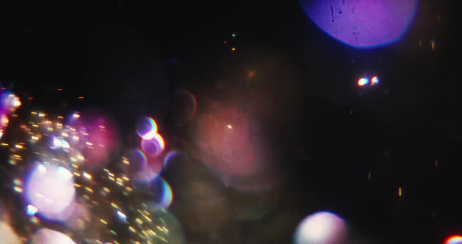 A dreamlike swirl of colorful, sparkling light leaks and bokeh drifts across a dark space
