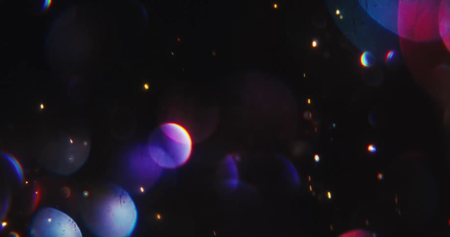 A magical swirl of vibrant, colorful bokeh and sparkling golden glitter particles dances across a dark background