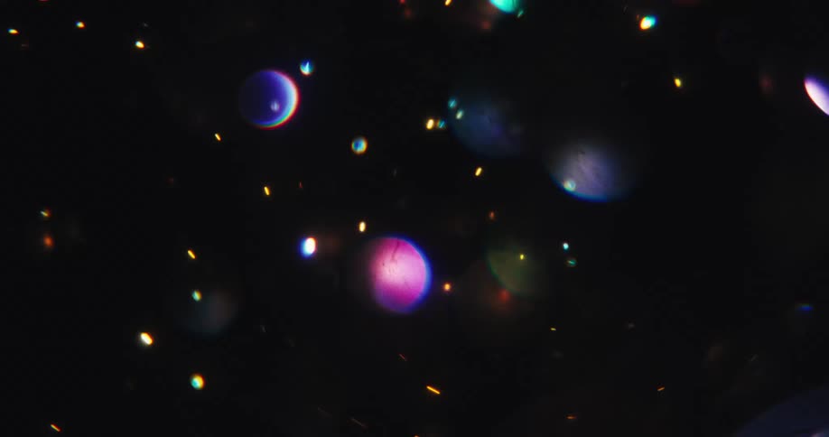 A magical display of colorful, shimmering bokeh and glitter particles float and streak across a dark background