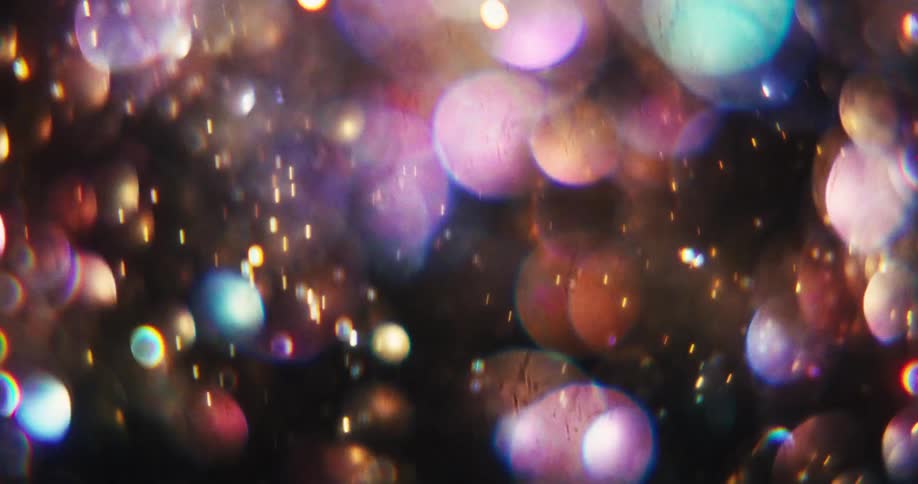 Abstract background of colorful, shimmering bokeh glitter and light particles floating and sparkling against a dark backdrop