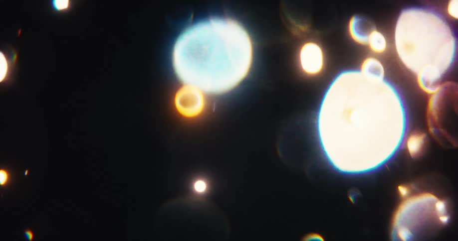 Shimmering orange and red bokeh lights and sparkling particles dance and drift across a dark background