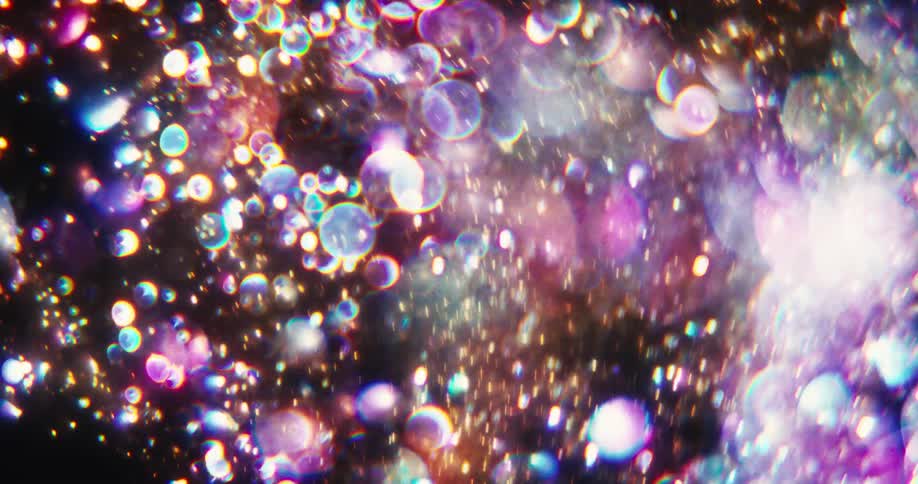 A celestial cascade of shimmering, multicolored bokeh and glitter particles drifts through the darkness