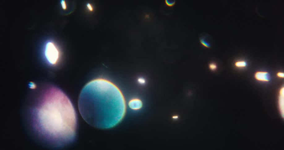 A dreamy dance of abstract bokeh lights and lens flares in shifting warm and cool tones against a dark background