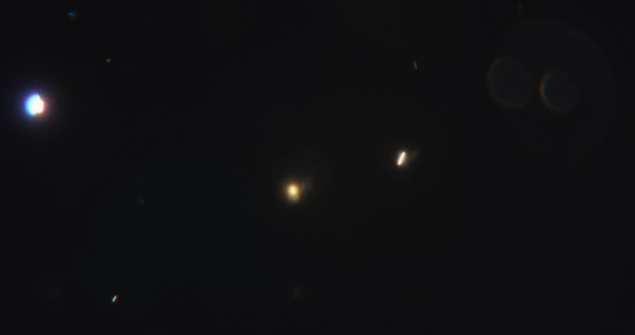 A mesmerizing journey through a sea of colorful, abstract bokeh lights and particles that float and drift across a transitioning background from warm orange to deep black