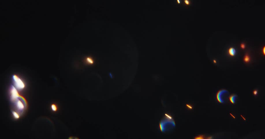 Colorful glowing particles and sparkling bokeh shimmer and streak across a dark background