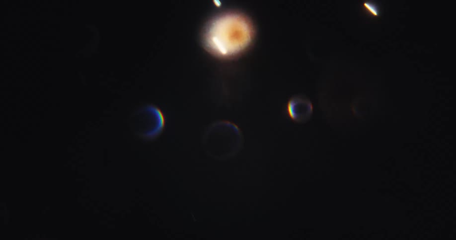 A mesmerizing display of abstract, multicolored bokeh lights and lens flares drifts and pulses in the darkness