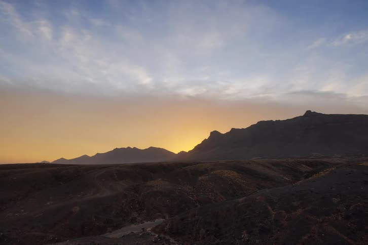 A time-lapse captures the golden sun rising majestically from behind a silhouetted desert mountain range
