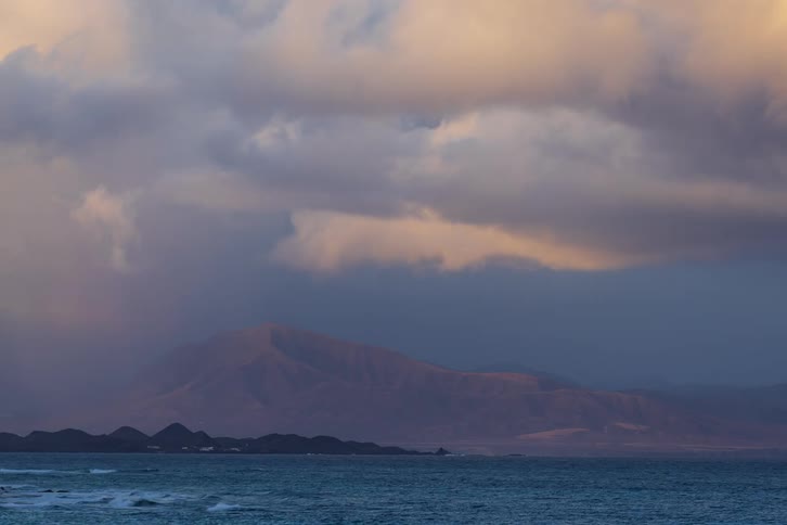 Dramatic sunset timelapse of storm clouds moving over sun-kissed mountains across the ocean