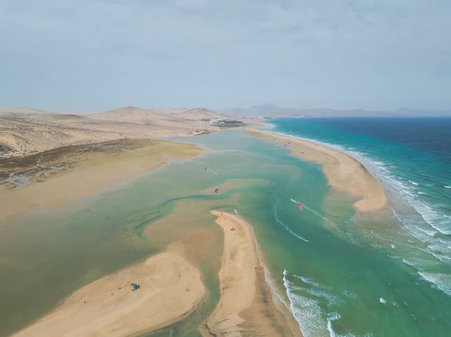 An expansive aerial view reveals kitesurfers gliding across a stunning turquoise lagoon next to a sandy desert coastline