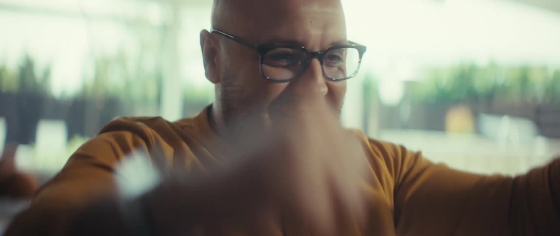 A happy bald man with glasses celebrates a victory in slow motion, raising his arms in triumph inside his home