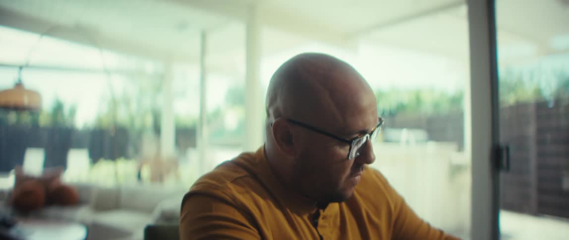 A focused man in glasses works remotely on his laptop from the comfort of his modern home