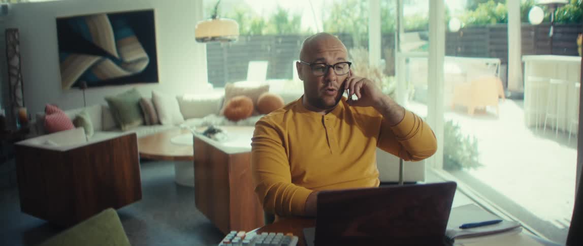 Businessman working from home on his laptop and talking on a cell phone in a modern living room
