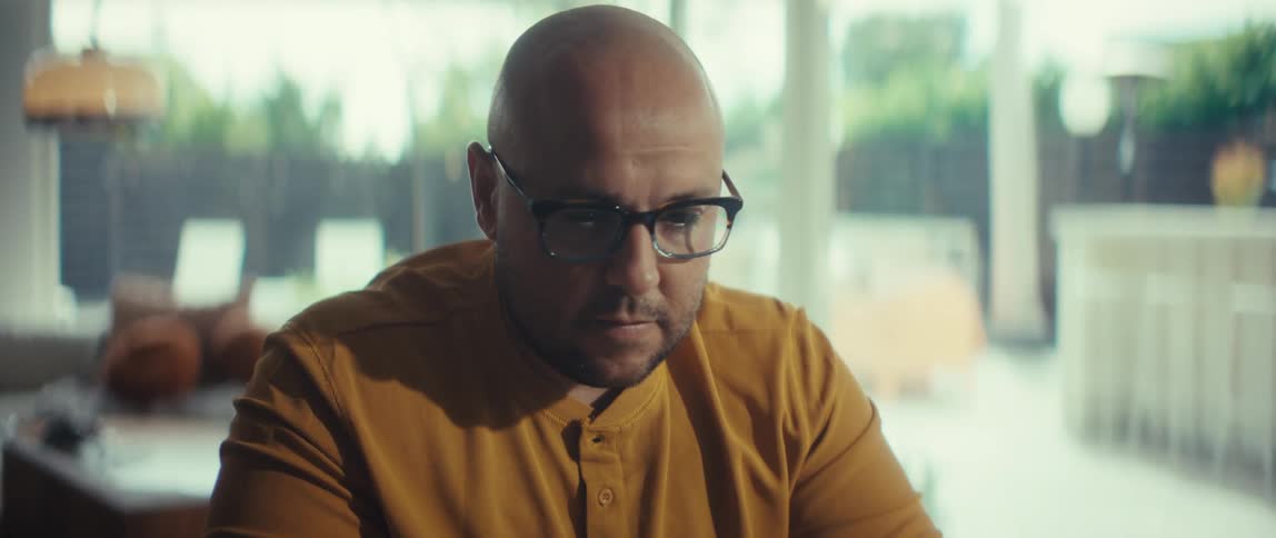 A close-up shot of a serious, bald man with glasses concentrating intently while working from his modern home