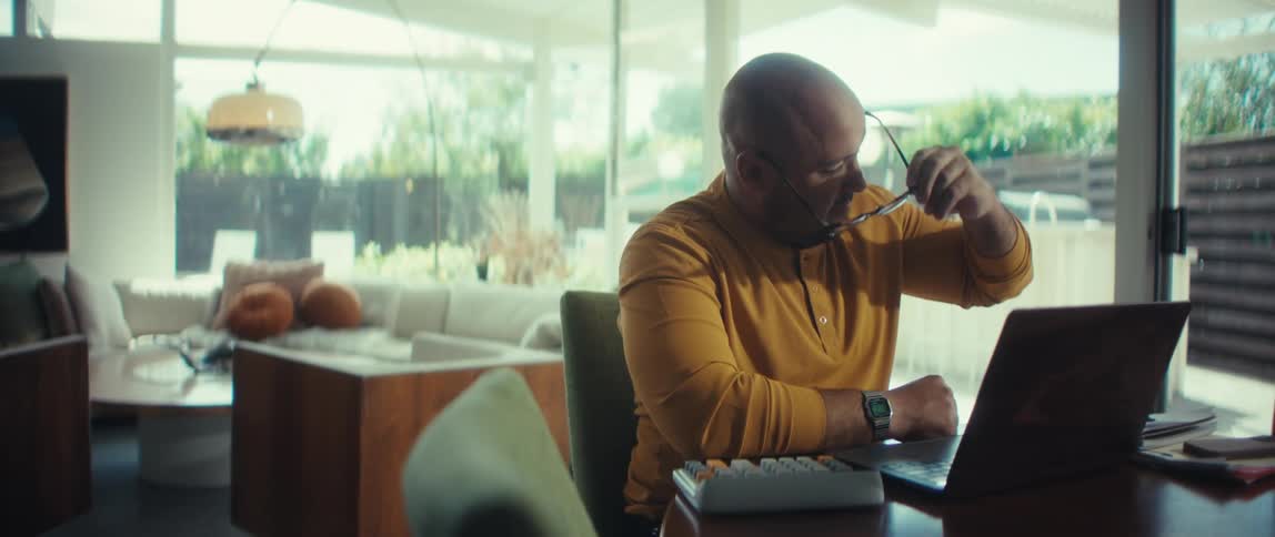 A man working from home smiles and waves goodbye on a video call before taking off his glasses and rubbing his tired eyes