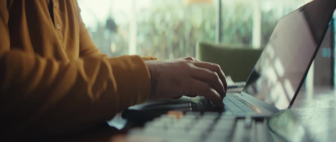 Slow motion close-up of a person's hands opening a laptop and beginning to type on a wooden desk