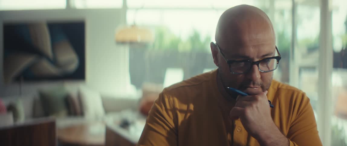 A focused man working from home thinks deeply about a problem before looking up with a satisfied smile