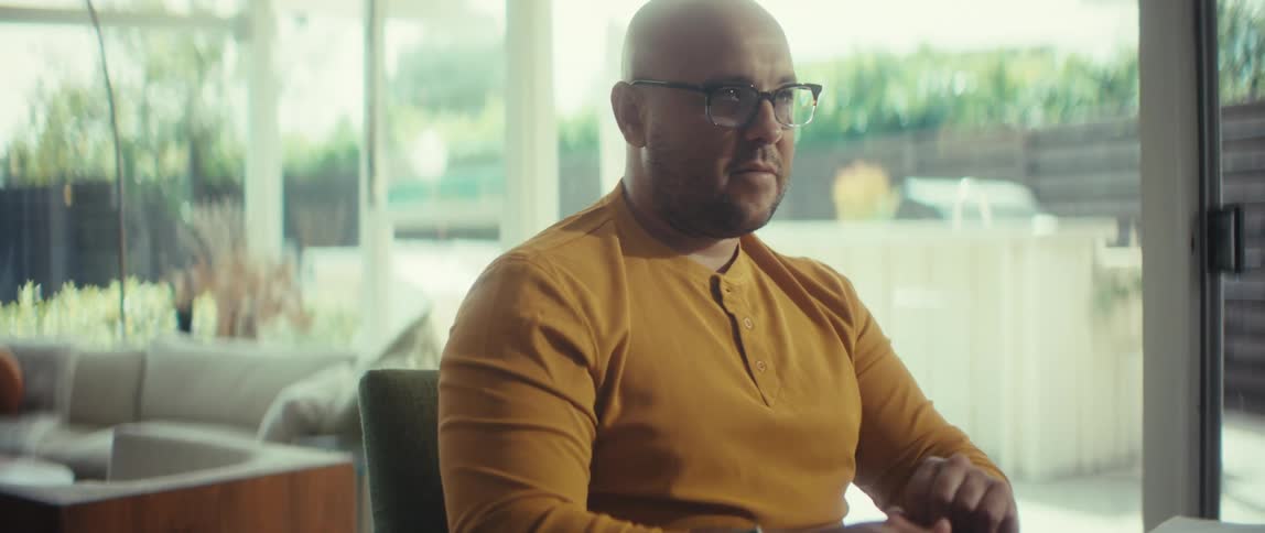 A pensive man in a yellow shirt finishes his work for the day, closing his laptop while working from his bright, modern home