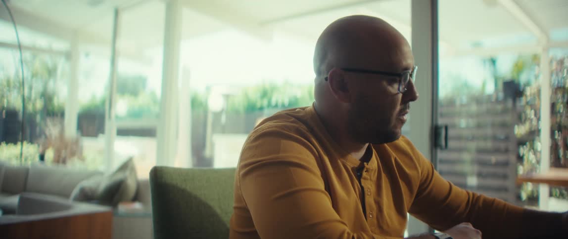 Slow motion dolly-in shot of a focused man in a yellow shirt working from his bright modern home, taking notes from his laptop