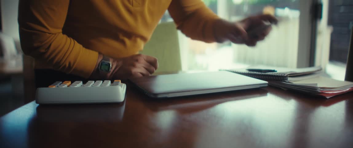 A man sits down at his dining room table in his modern home and opens his laptop to begin working