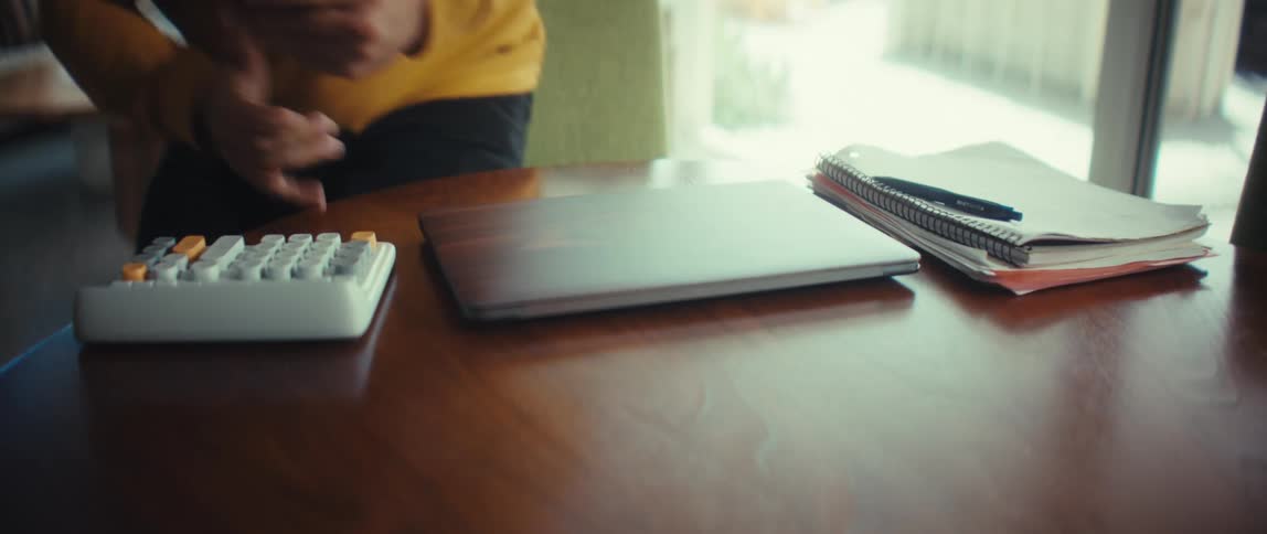 A man finishes working from home in his modern living space, closing his laptop and walking away from the table