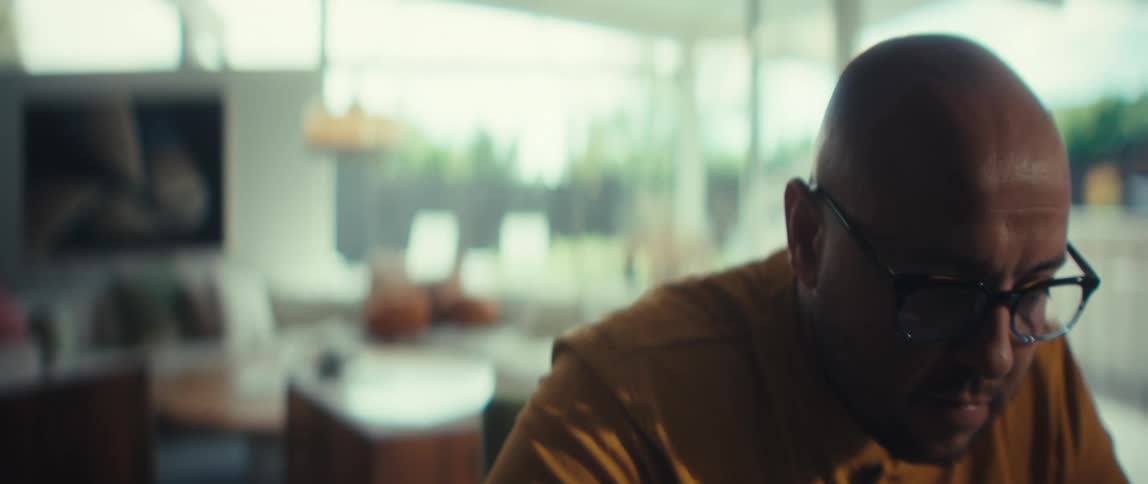 Slow zoom on a focused man with glasses in a modern home, working on his laptop and writing with a pen