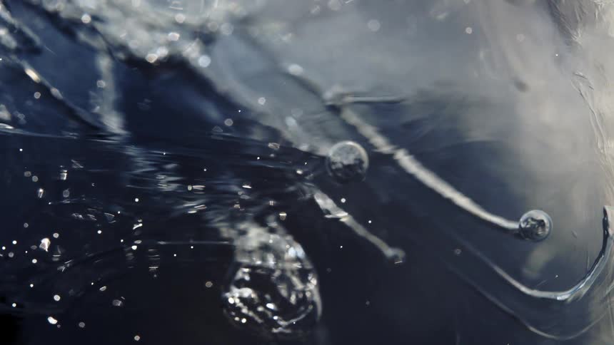 An abstract macro cinemagraph shows tiny air bubbles and particles shimmering and moving within a block of dark, frozen ice