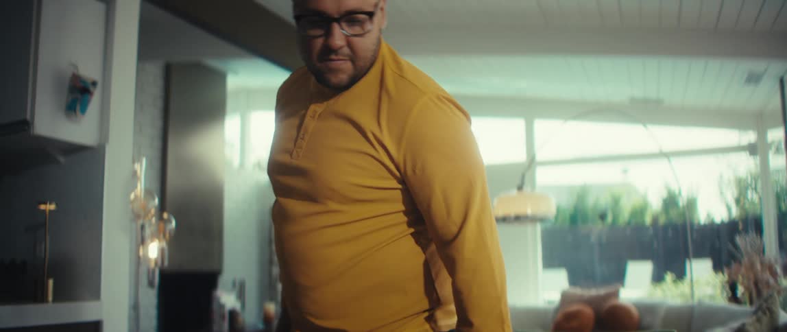 A man wearing glasses and a yellow shirt closes his laptop after working from home in his stylish, modern dining room and walks away