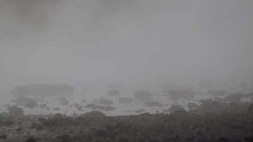 A mysterious scene of thick steam billowing over a rocky geothermal landscape