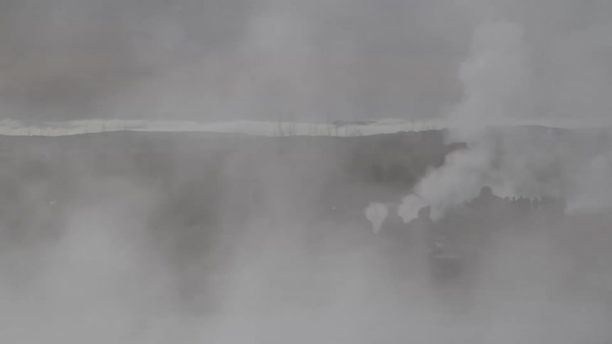 Thick white steam billows from a geothermal area, creating a foggy and mysterious landscape with distant silhouettes