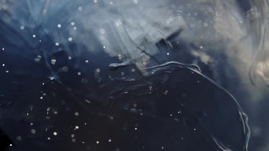 An ethereal macro shot of dark, inky liquid swirling in slow motion with shimmering bubbles and particles, creating a mysterious, cosmic effect