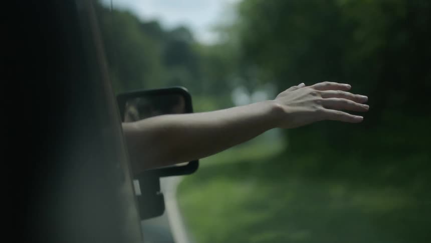 A person hangs their arm out of a moving car on a cloudy day