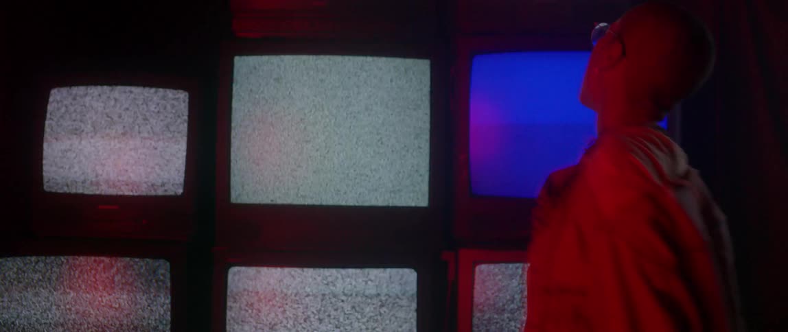 A person with glasses bounces around static filled television sets