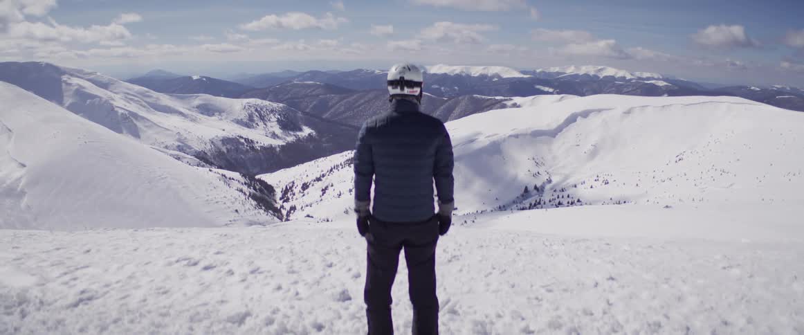 Rear view of a skier standing on a snowy mountain top and enjoying the panoramic view of the winter landscape