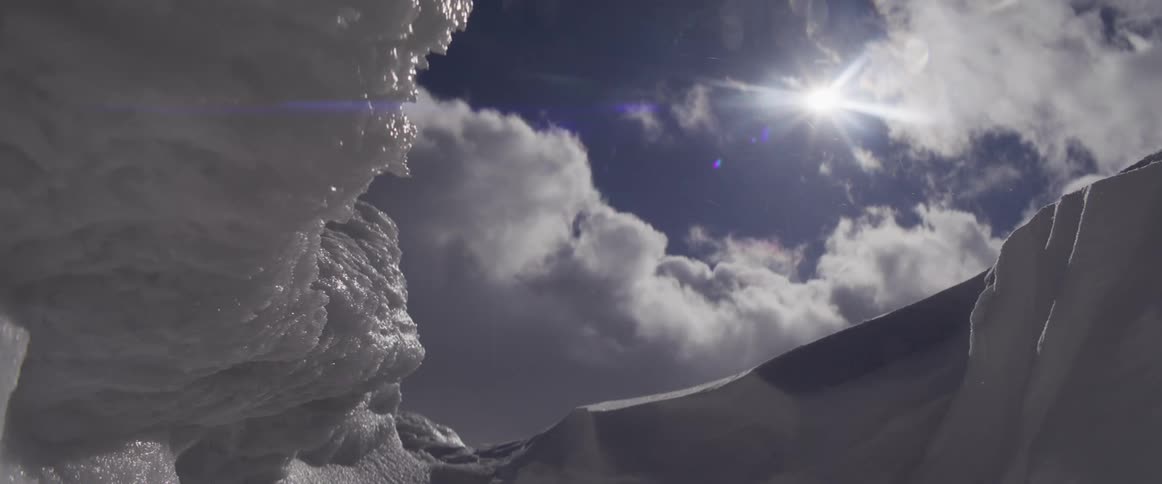 Low angle view of the sun shining brightly above a frozen, icy landscape as snow crystals blow in the wind