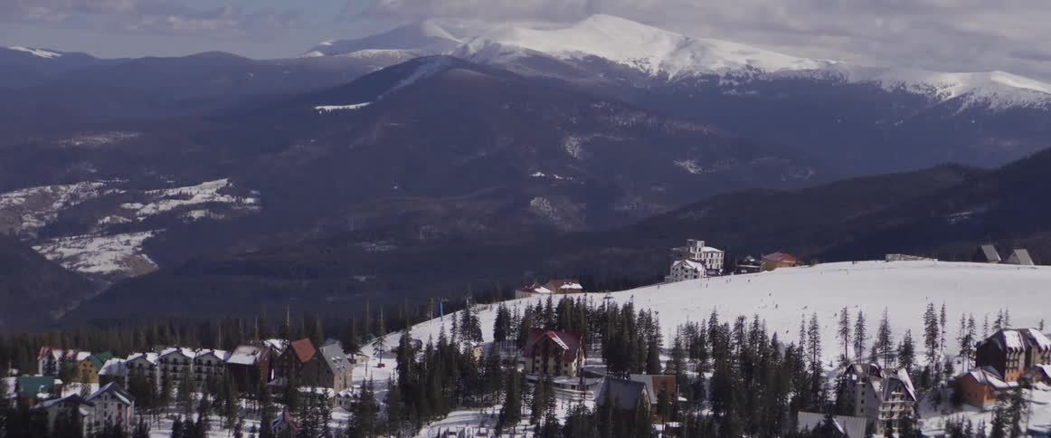 A scenic view of a ski resort village on a snowy mountainside, with majestic snow-capped peaks in the distance