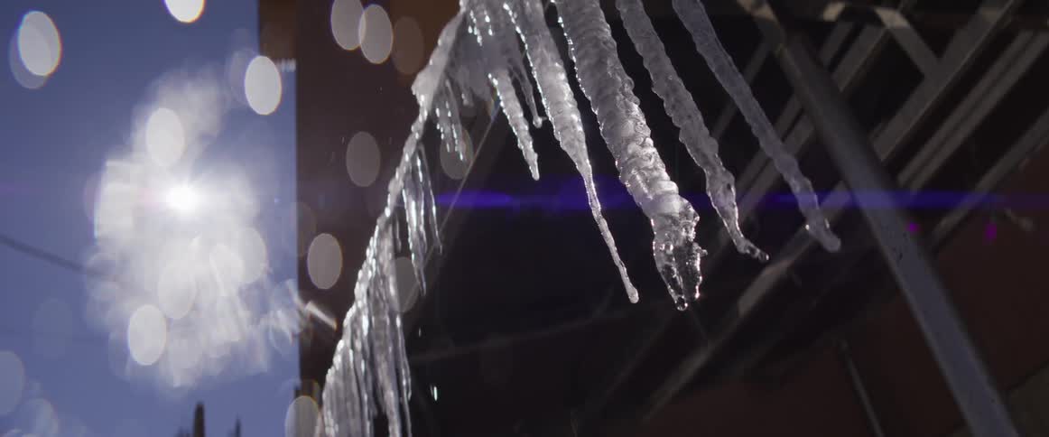 Slow motion close-up of icicles melting and dripping water as the bright sun shines in the background