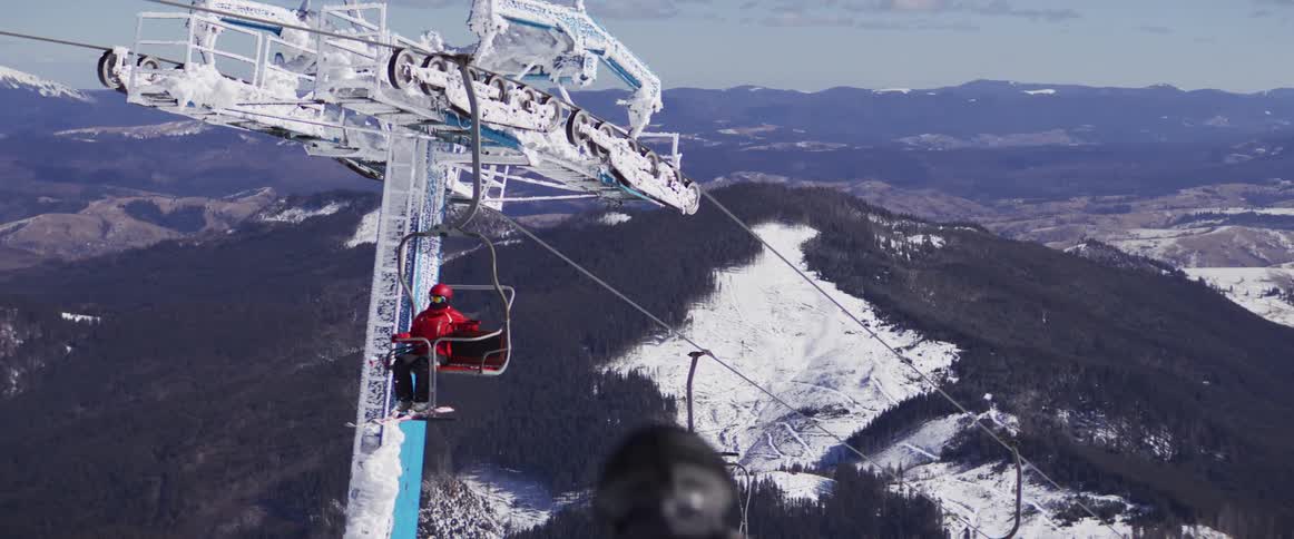 Close-up of a frozen ski lift mechanism with a skier riding a chair up the mountain slope