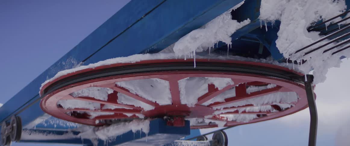 A close-up of a massive red ski lift wheel covered in snow and ice slowly turning on a frosty winter day