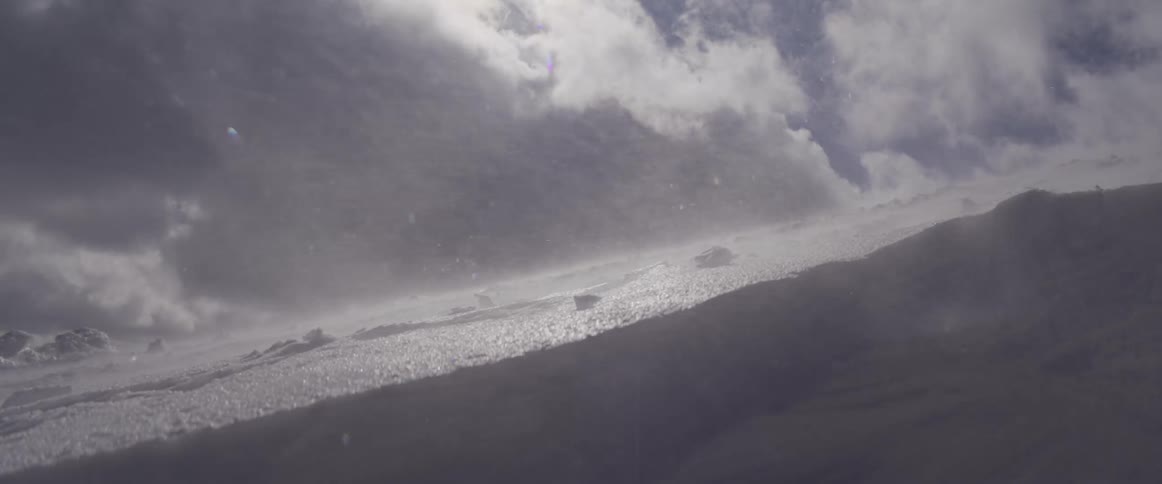 Slow motion shot of a fierce blizzard with snow blowing across a sunlit, snow-covered mountain