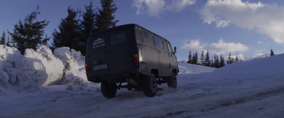 Slow motion view of a rugged van driving up a winding, snow-covered mountain road on a sunny winter day
