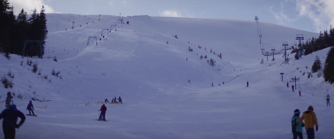 Distant view of a lively ski slope with numerous people enjoying winter sports under a bright sky