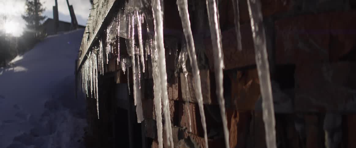 Shimmering icicles hang from a brick building's roof, slowly melting and dripping in the bright winter sunlight
