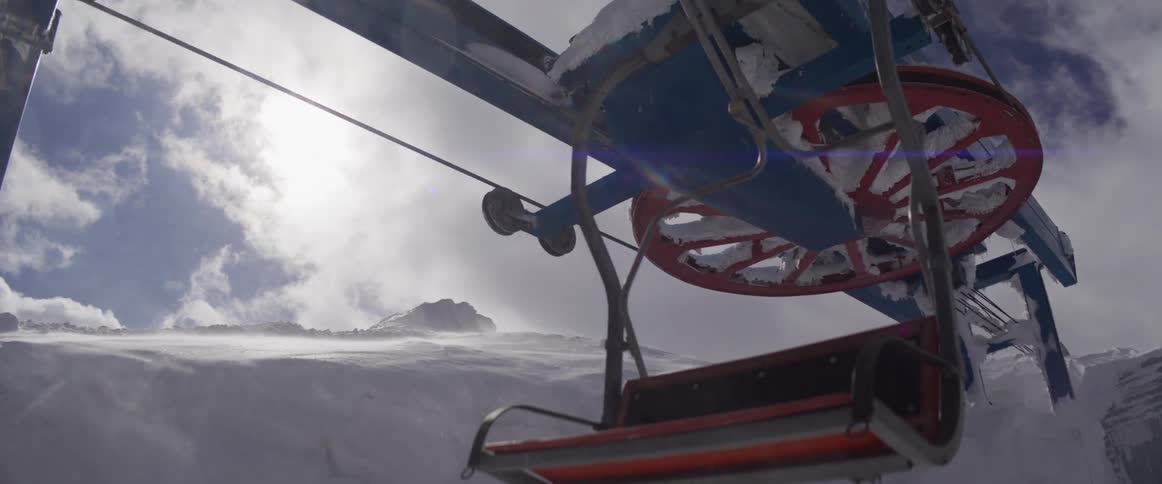 A slow-motion close-up of a snow-covered ski lift operating on a windy mountain as empty chairs pass by