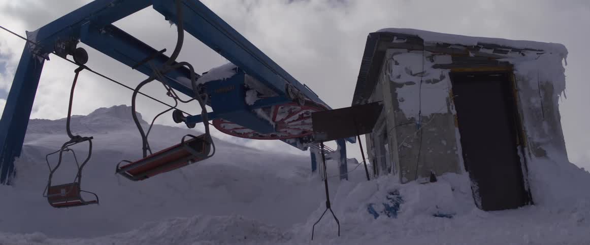 An old, abandoned ski lift sits motionless next to a dilapidated hut on a snowy mountain