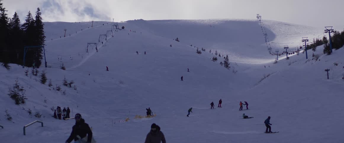 Skiers and snowboarders enjoy a day on the slopes of a busy mountain resort with ski lifts in the background